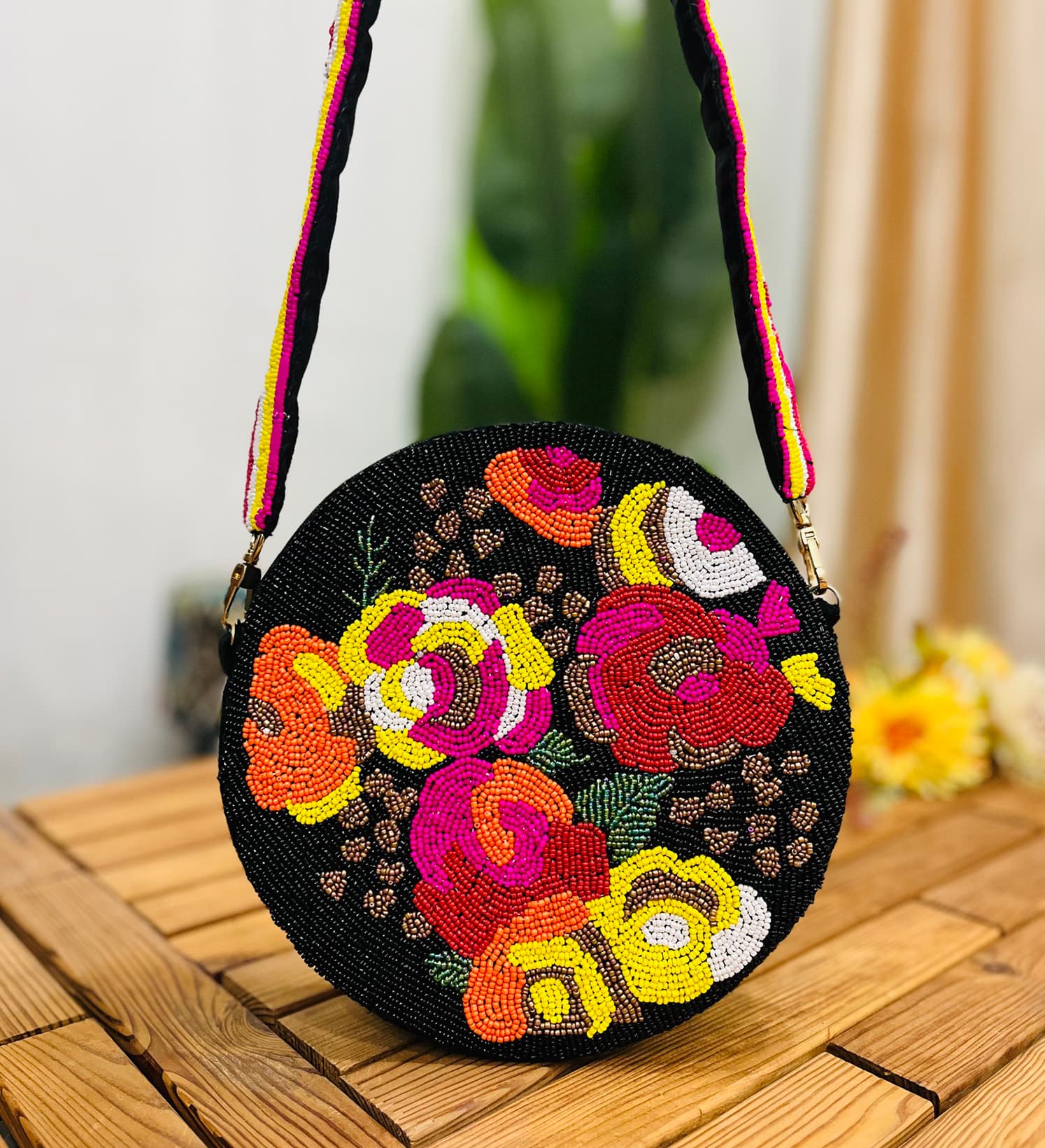 A black circular shoulder bag with intricate hand-beaded patterns in vibrant colors, featuring a long black strap.